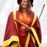 A woman in a graduation gown and cap proudly holds her diploma, celebrating her academic achievement.