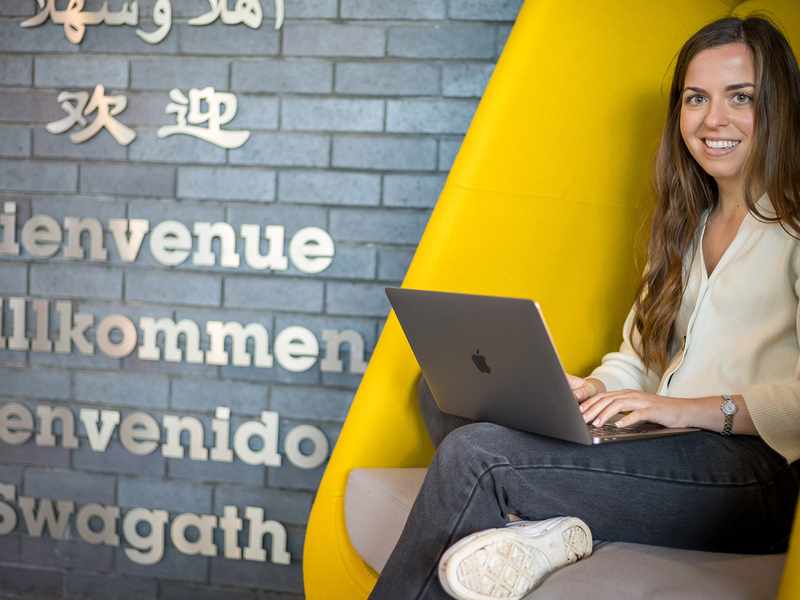 A woman working on her laptop while comfortably seated in a bright yellow chair, showcasing a lively atmosphere.