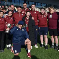 A diverse group of people posing on a rugby field, showcasing camaraderie with a bright green field behind them.