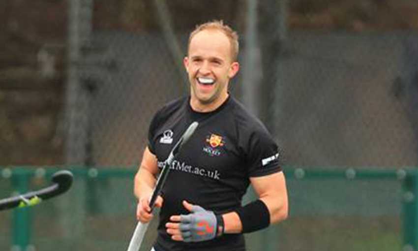 Luke Hawker stands smiling holding a hockey stick during a game