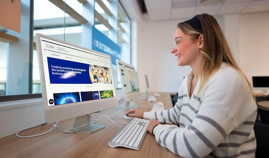 A person sat at a desk in front of a Mac computer.