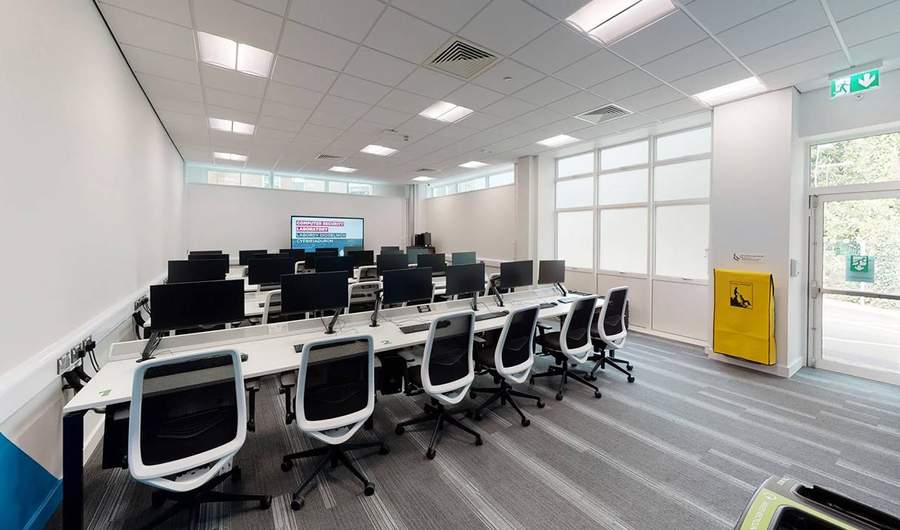 Rows of desks with computer screens and desk chairs.