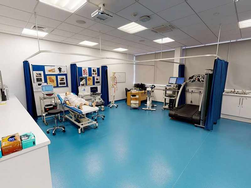 A large room with a height-adjustable bed, treadmill, and medical diagnostic equipment.