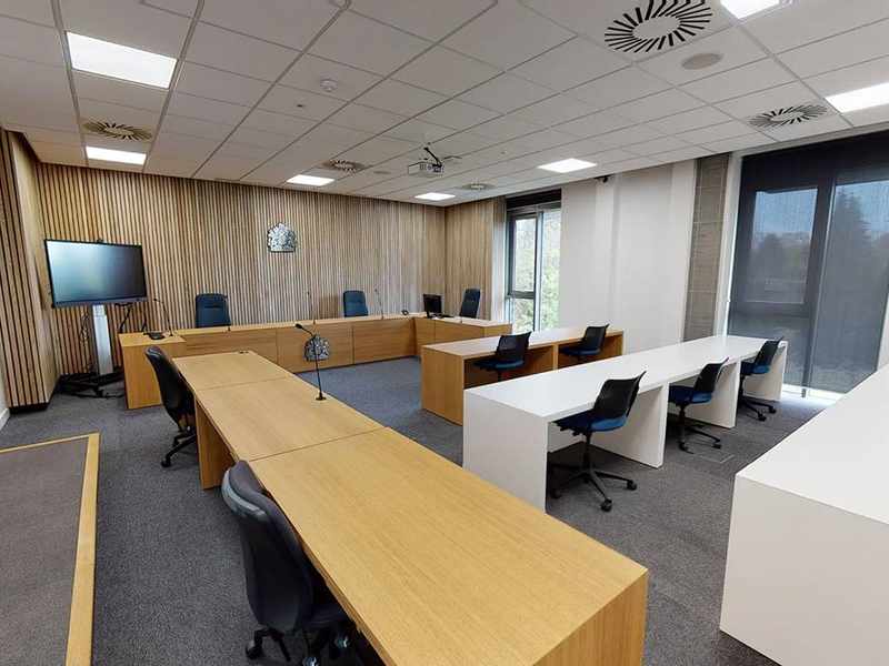 A large room with desks and chairs arranged in rows. At the far end is a long desk with a crown symbol mounted on it.