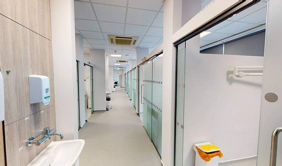 A long brightly lit corridor. Along the right are several small rooms with frosted glass doors.