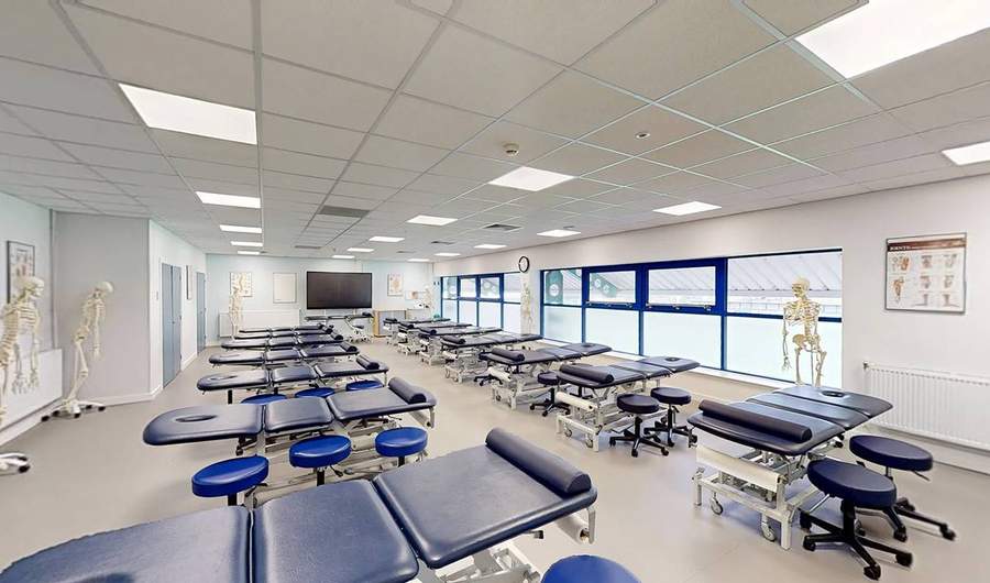 A large, brightly lit room with two rows of massage tables.
