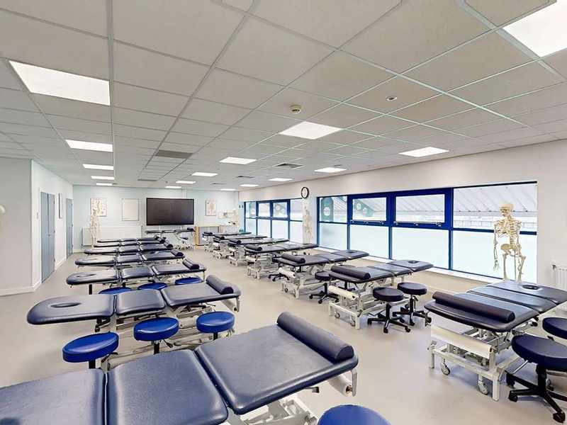 A large, brightly lit room with two rows of massage tables.