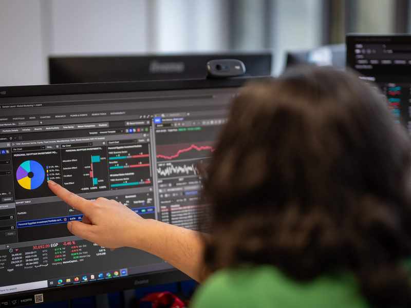 A person points to a large computer monitor showing financial charts.