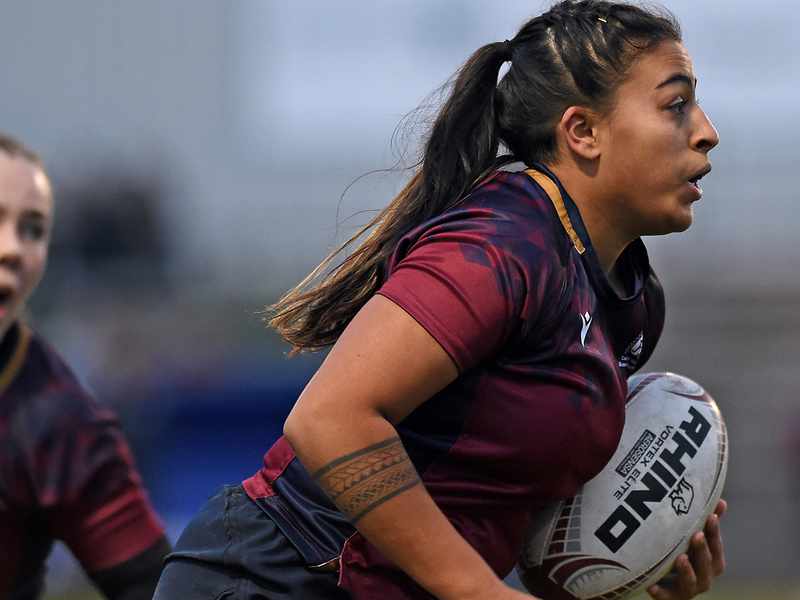 Two women in maroon jerseys engaged in a rugby match, showcasing teamwork and athleticism on the field.
