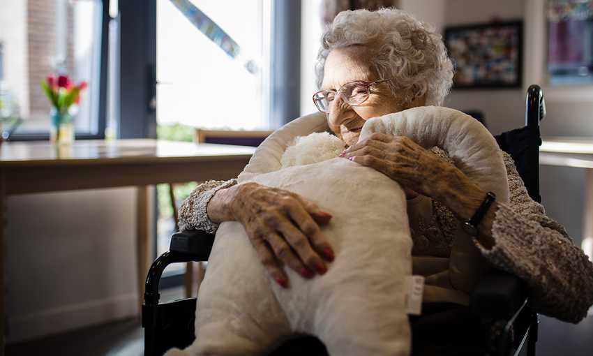 Woman in wheelchair hugs a large white teddy bear