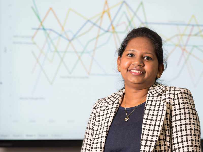 A person stands in front of a large screen showing line charts.