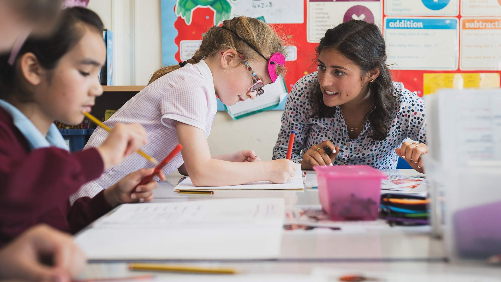 A woman sits on the floor with a young child who is playing on a unicorn ride-on toy. The room is decorated with colorful toys, wall stickers of trees and animals, and foam play mats. The atmosphere is playful and engaging.