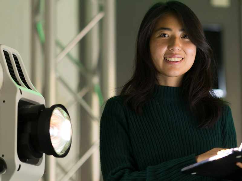 A woman with a laptop in hand is positioned in front of a gentle light, highlighting her concentration and intent.