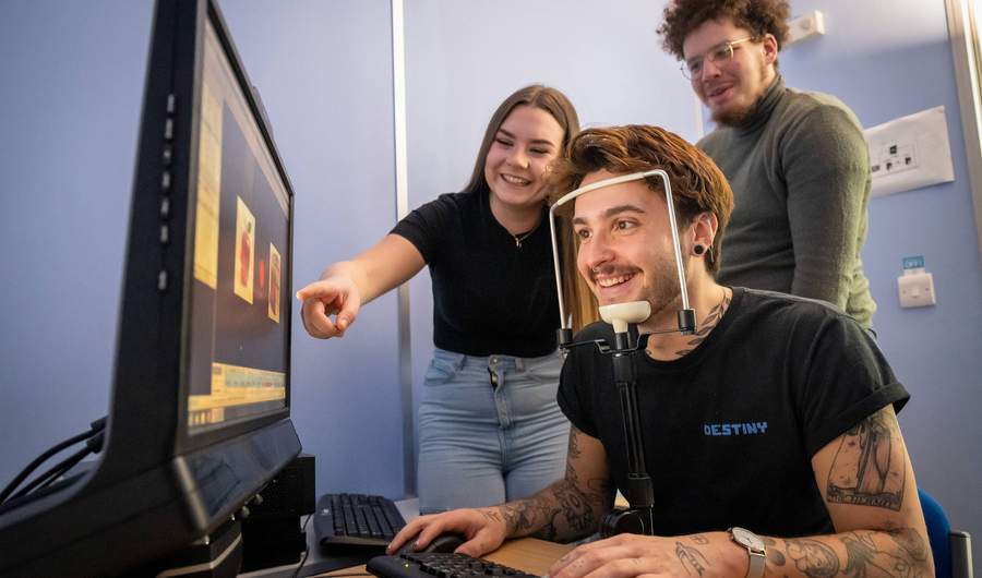 A person sits facing a computer screen. Their chin is resting on a stand.