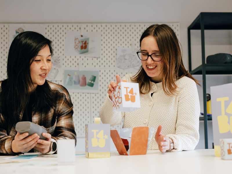 Two women engaged in conversation while seated at a table, with paper boxes placed between them.