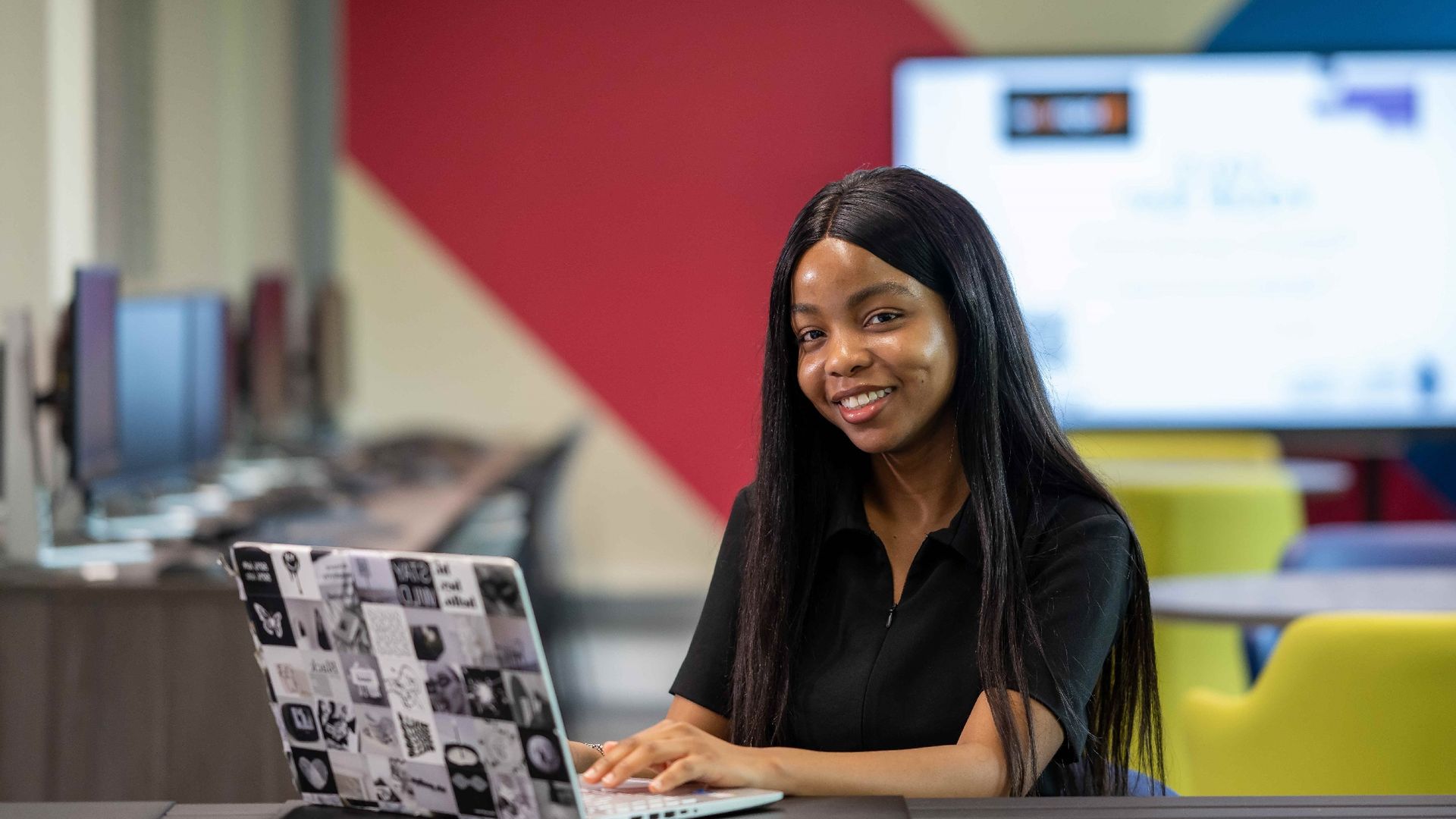 A young woman sits at a desk and works on their laptop