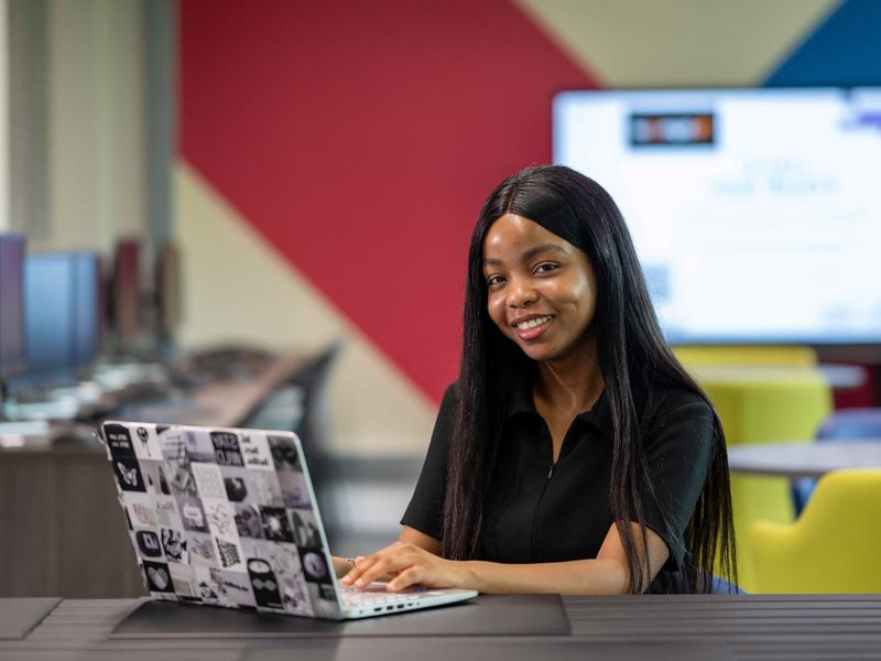 A young woman sits at a desk and works on their laptop