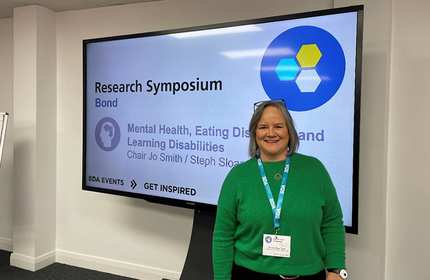 A woman poses in front of a large screen, likely showcasing information or visuals.