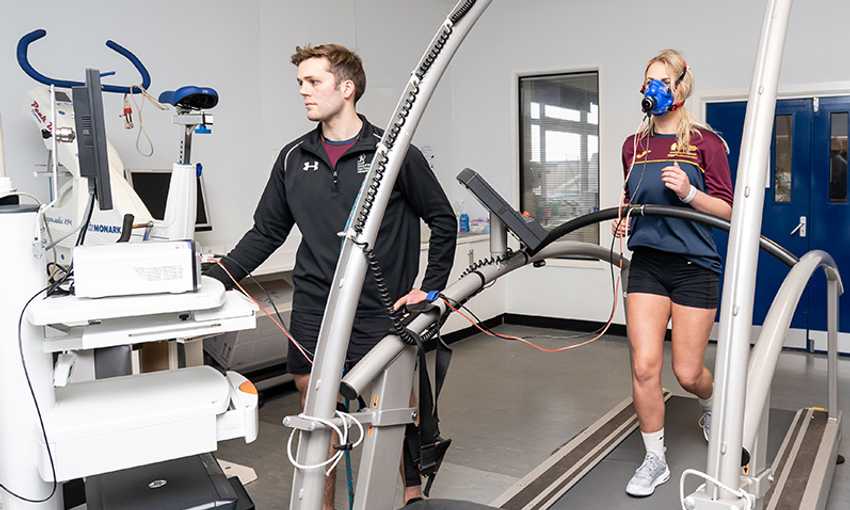 A student walks on a treadmill wearing a breathing mask while a researcher monitors physiological responses.