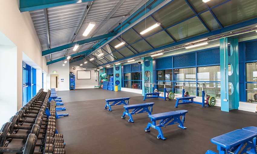 A spacious gym with blue benches, dumbbells, and open workout areas.
