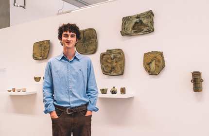 A person stands in front of a display of ceramic objects. Some are sitting on shelves, while others are mounted on a wall.