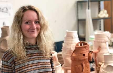 Elin Hughes standing in front of table of ceramics artwork