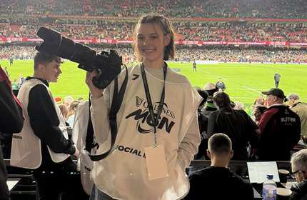 A young woman holds a camera with a large lens in the stands at a sport stadium