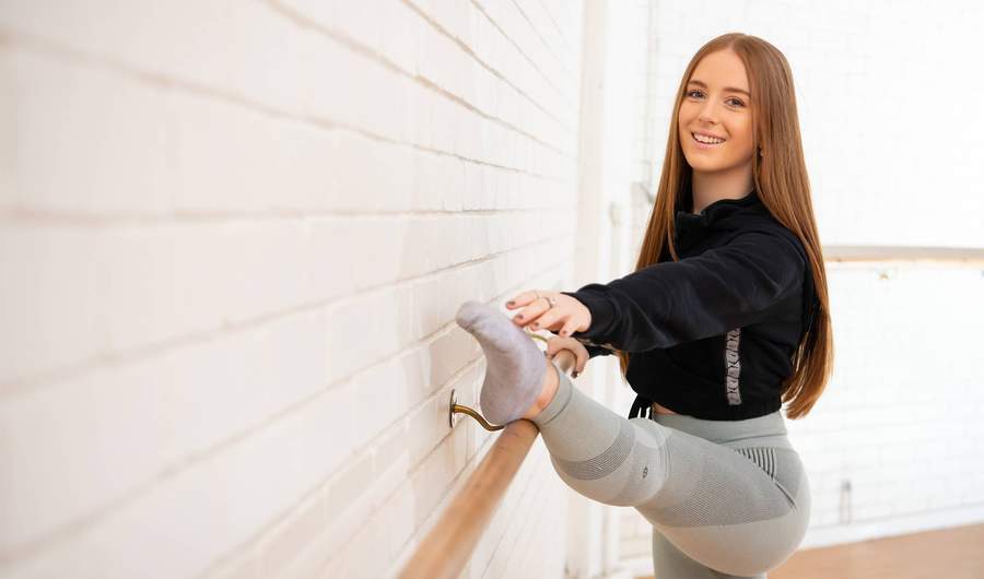 A person stretching their leg on a ballet barre in a dance studio.