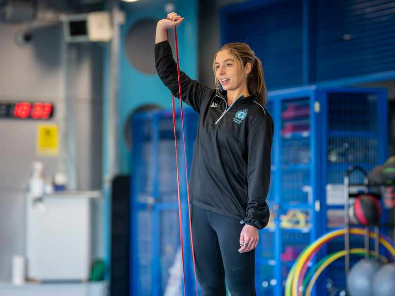 A person in a dark blue tracksuit stretches a red exercise band.