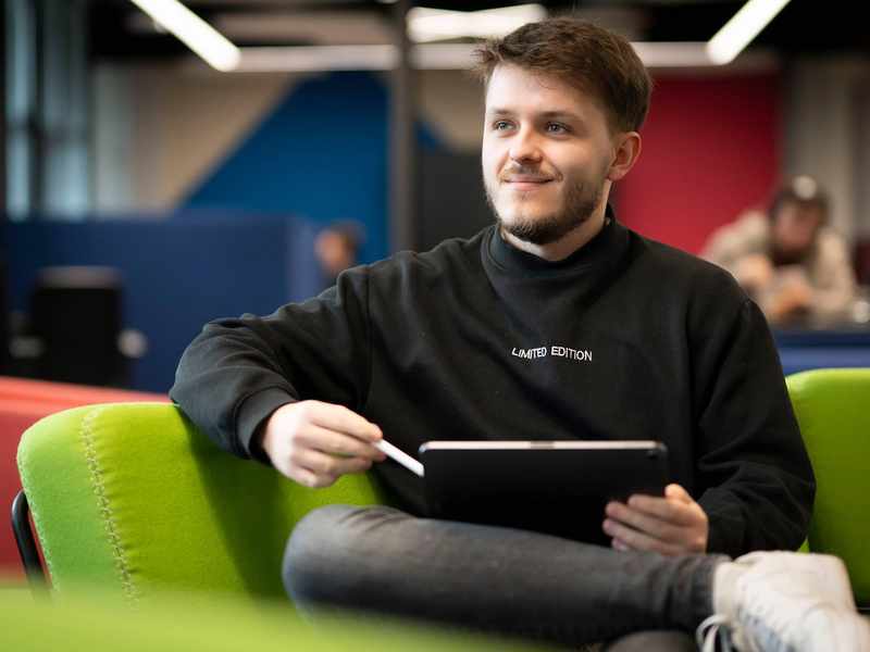 A person sits on a couch with a tablet computer resting on their knee.