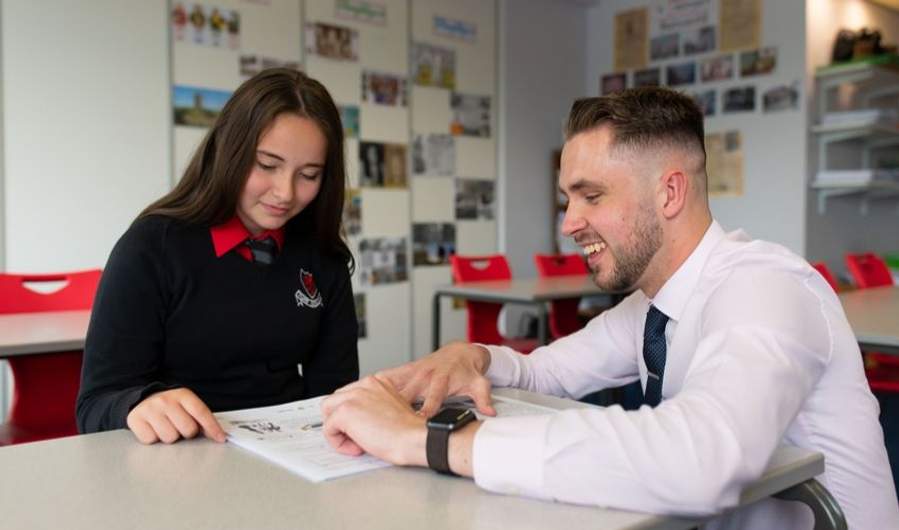 Sion Davies leans down on a table to help a pupil with their work