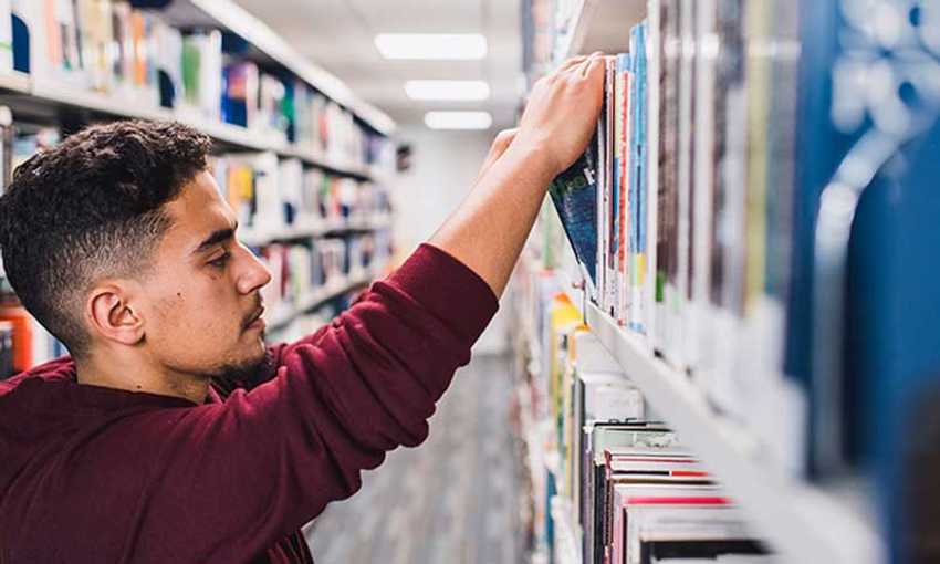 Side view of a student reaching for books on the shelves