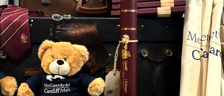 A display of Cardiff Metropolitan University merchandise, including branded plush bears, tote bags, and ties