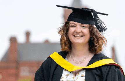A smiling woman wearing a graduation gown, celebrating her achievement on graduation day.