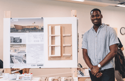 A man stands beside a poster board displaying an image of a building.