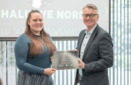 A man and woman proudly hold an award in front of a large screen displaying text or images.